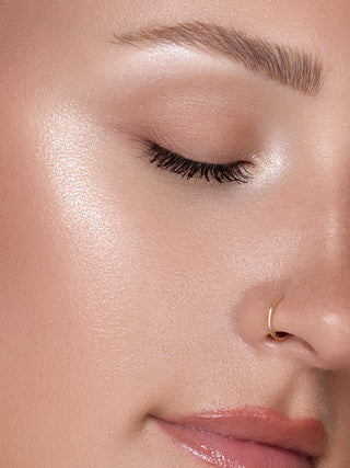 Close-up of a woman's eye with a subtle makeup look and gold nose ring Shimmer Veil highlighter by Beauty Creations