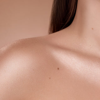 Close-up of a person's shoulder and neck with a neutral background showing Shimmer Veil highligther used on body.  Shimmer Veil Highlighter for Face and Body by Beauty Creations. Color payoff.