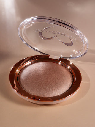 Compact powder in a clear case on a beige background. Showing the open compact case of Shimmer Veil body and face highlighter by brand Beauty Creations.