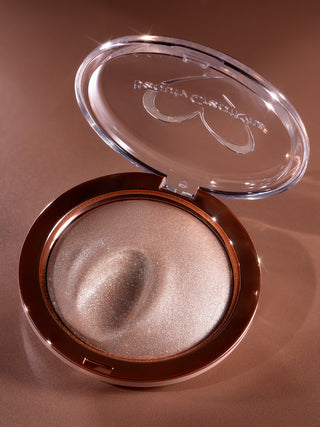 Compact powder with a visible brand logo on a brown background. Showing texture is soft and moldable body and face highlighter Shimmer Veil by brand Beauty Creations