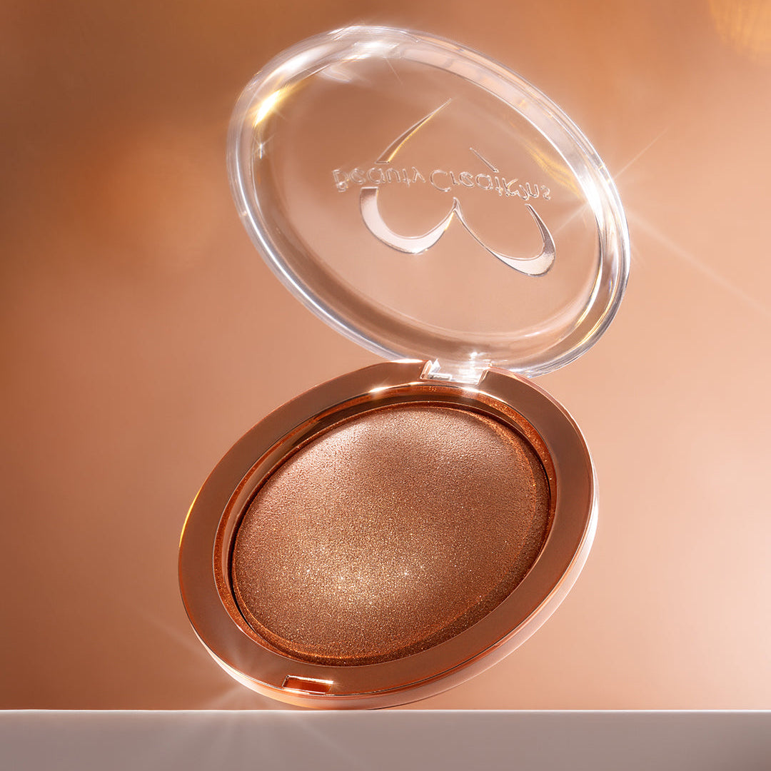 Compact powder in a rose gold case with a blurred background. Shade is Rose Gold Shimmer Veil Beauty Creations Face and Body Highlighter