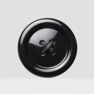A single glossy black button with a textured dark cord cross, centered on a light gray background.
