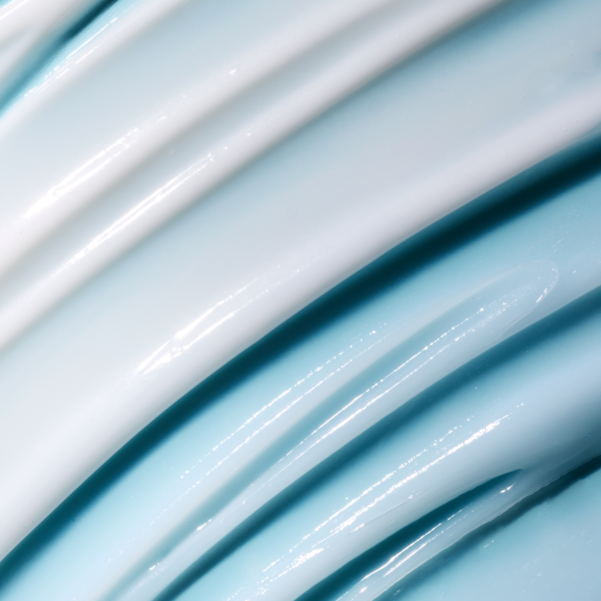 A close-up of glossy, thick cream or lotion swirled in diagonal layers, showing a pale icy blue and white color with a smooth, reflective texture.