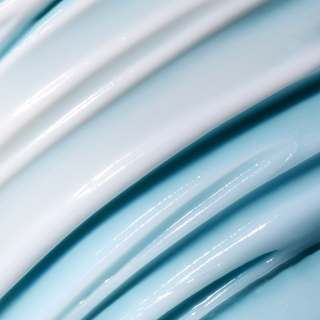 A close-up of glossy, thick cream or lotion swirled in diagonal layers, showing a pale icy blue and white color with a smooth, reflective texture.