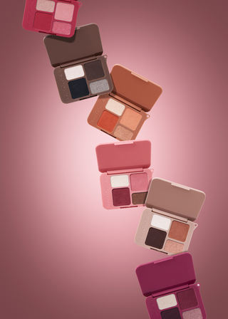 Six open eyeshadow palettes in various shades of pink, brown, and mauve are arranged diagonally against a matching pink gradient background.