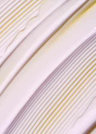 Close-up of a glossy ceramic plate with diagonal ridges and a shallow well, showing cream, white, and pale yellow tones with a subtle light purple cast.